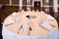 Banquet-room-with-white-place-settings-tables-with-fireplace-in-background